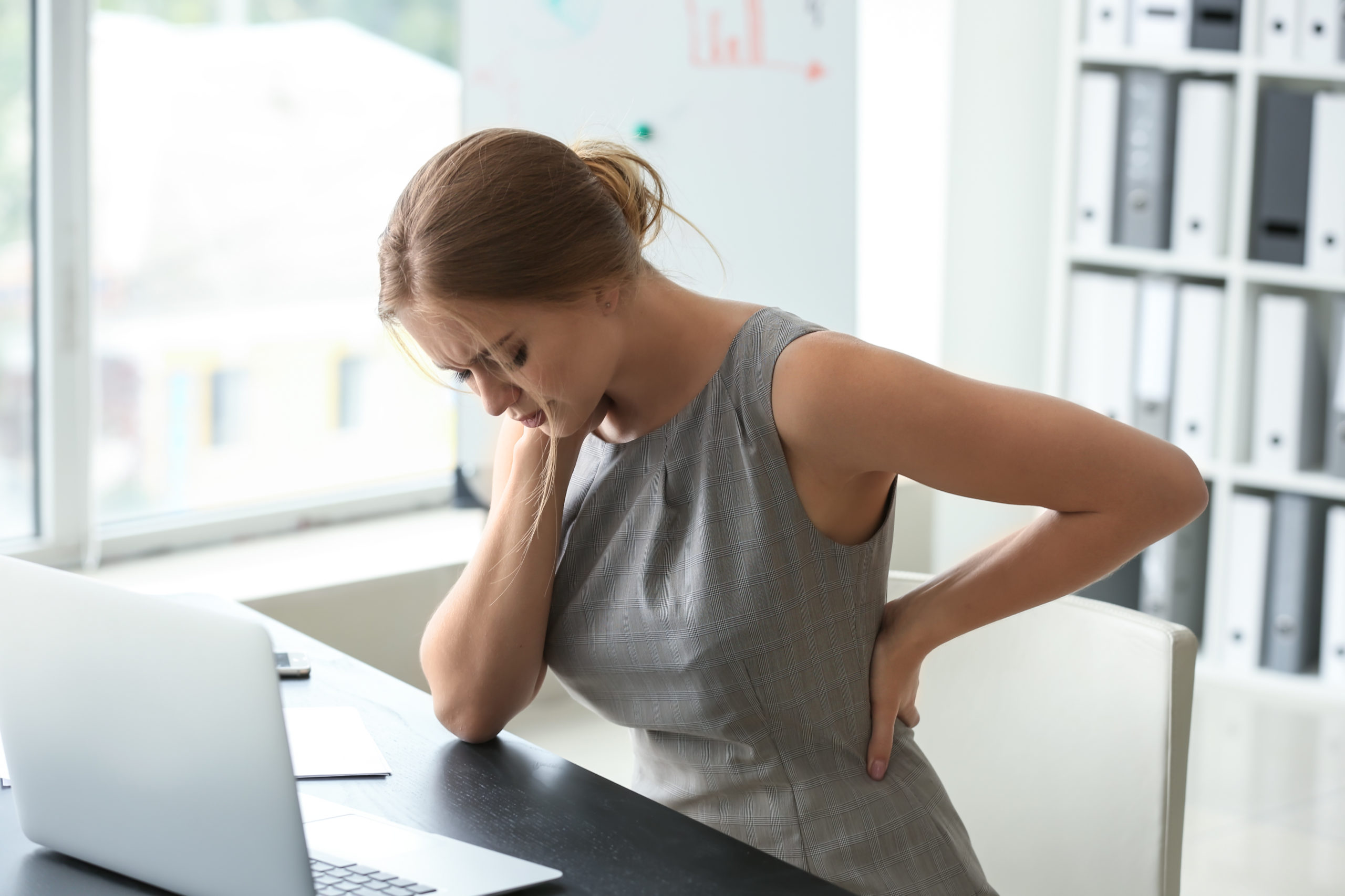 Young woman suffering from back pain in office